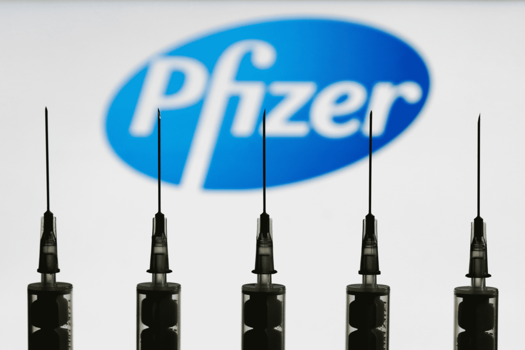 five syringes in focus with Pfizer in background
