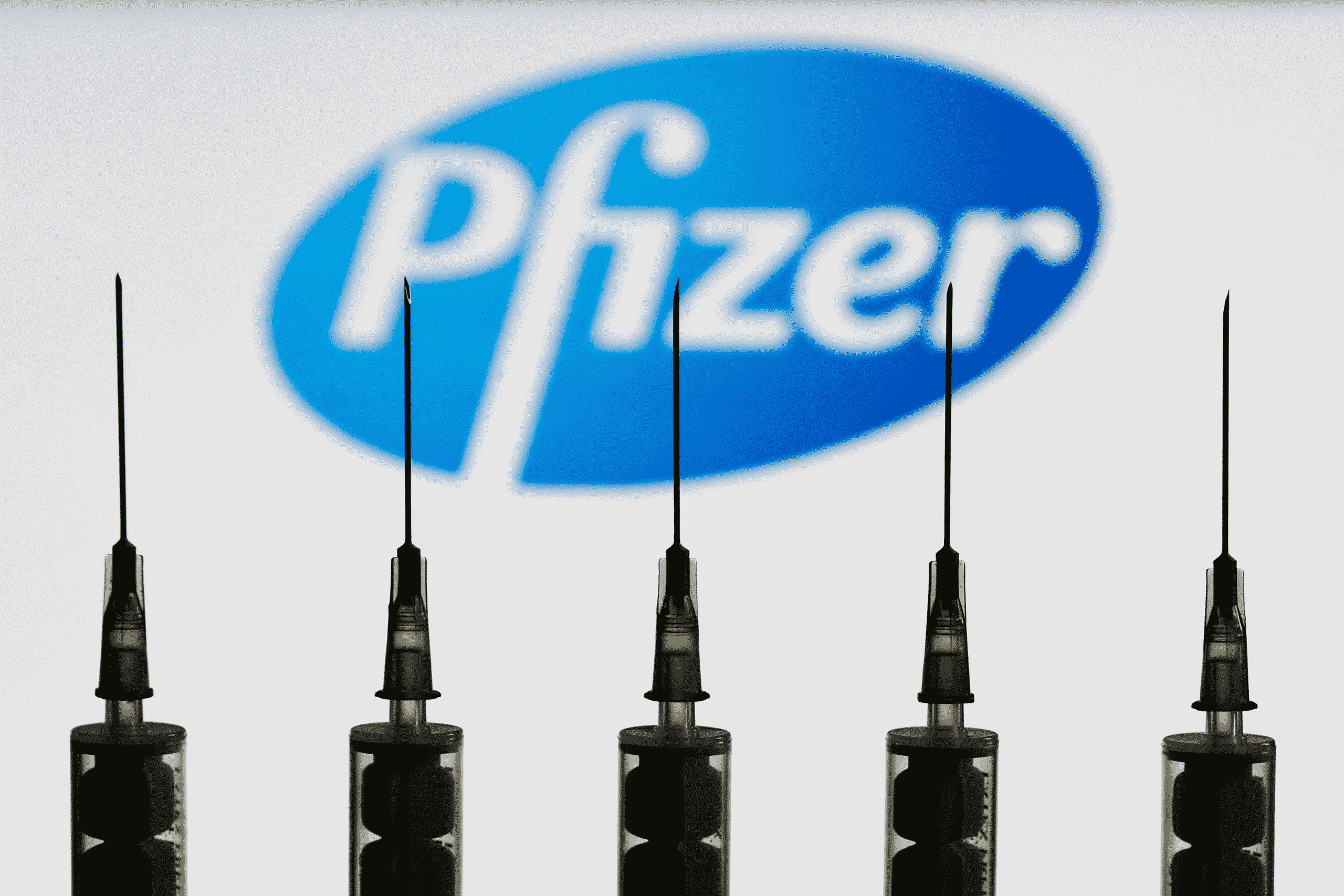 five syringes in focus with Pfizer in background
